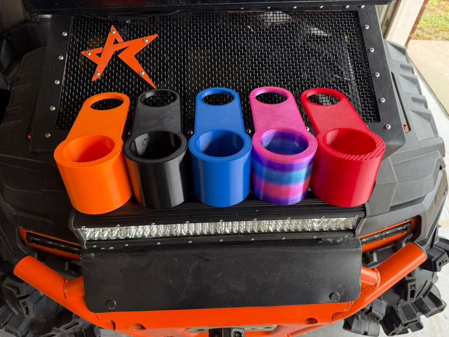 Five Polaris Sportsman 1000 cup holders in orange, black, blue, purple-blue swirl, and red on an ATV grille